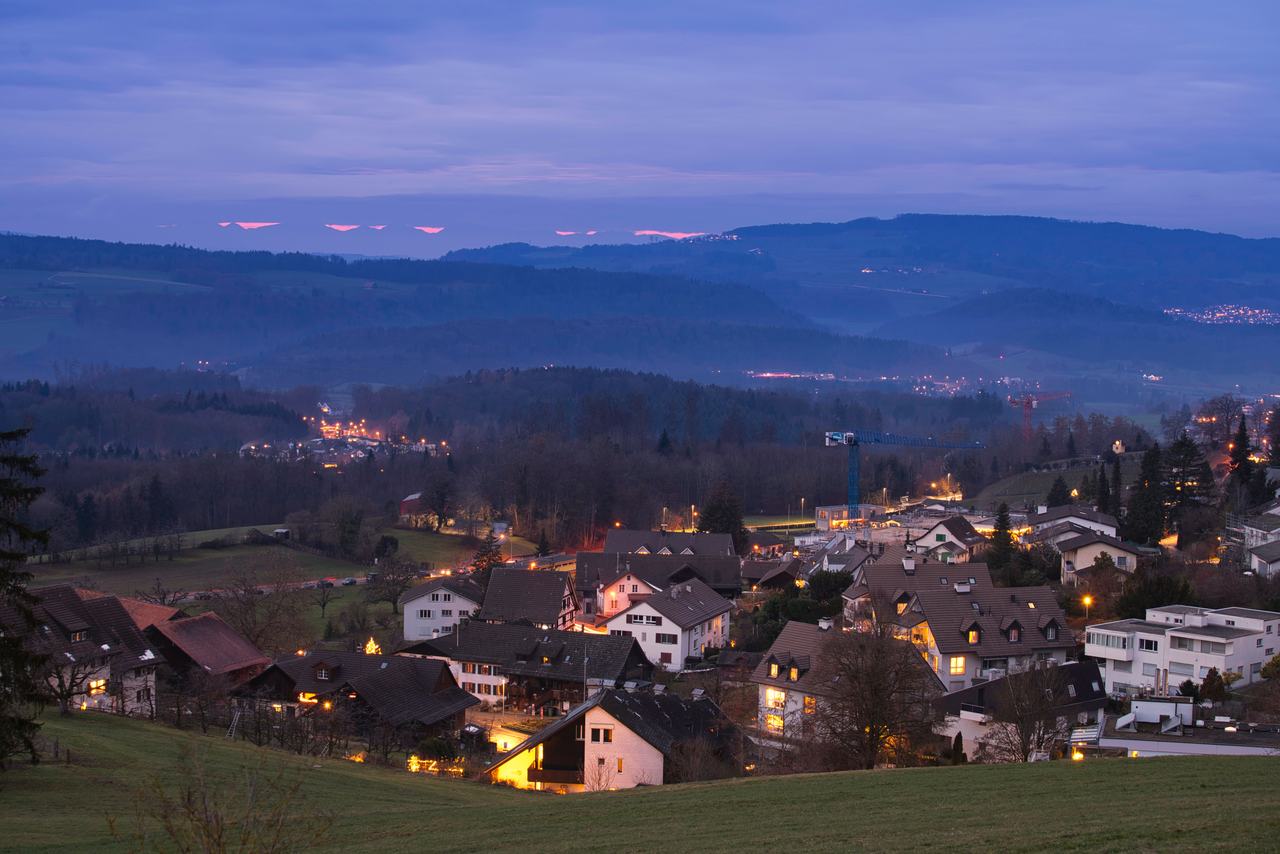 A village at twilight, house lights coming on below the hills